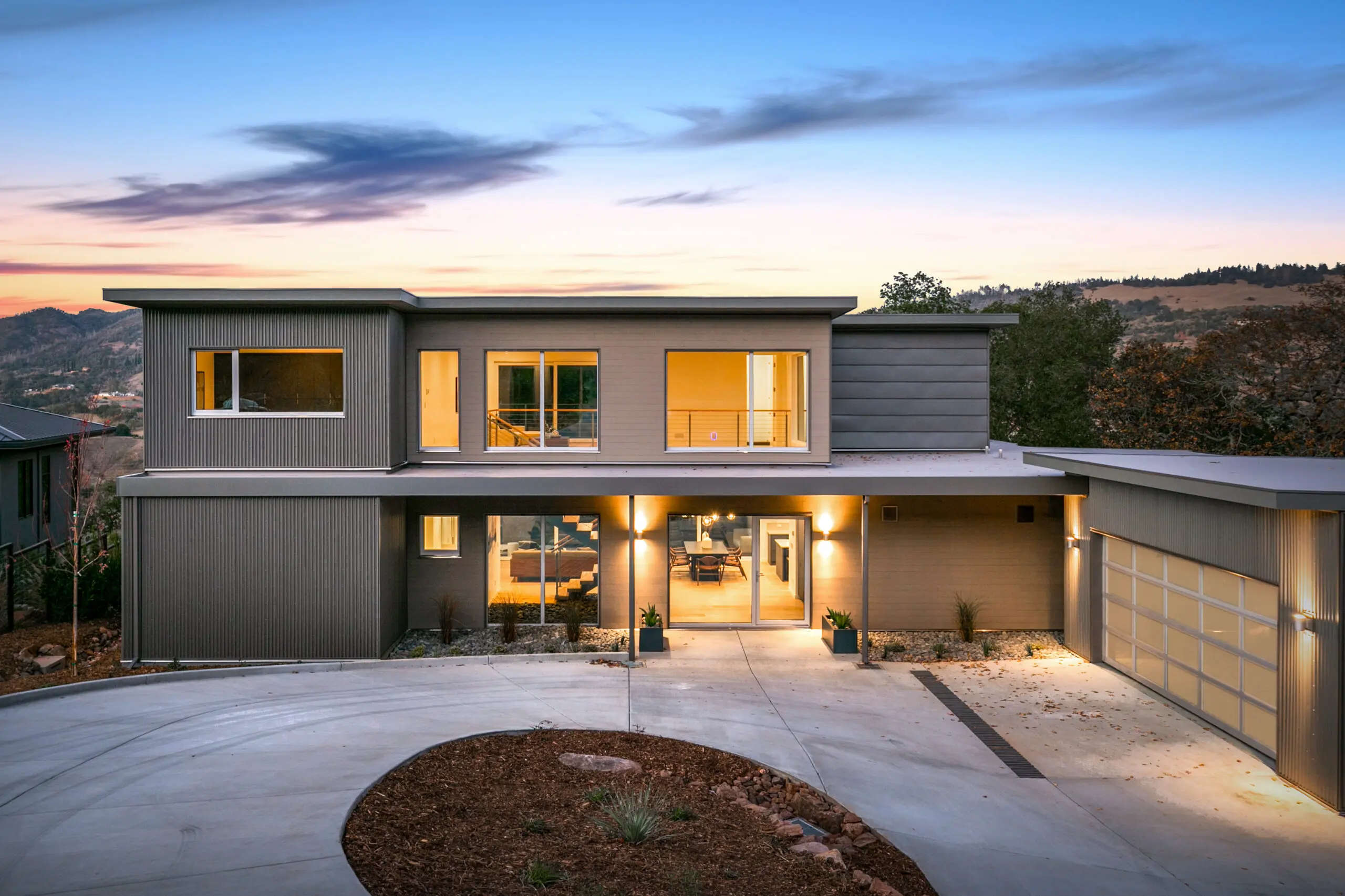 Dvele Shaughnessy Shelter Glen 2-story modern home with circular drive; sunset a scrub landscape in the background. Modular home by Dvele.